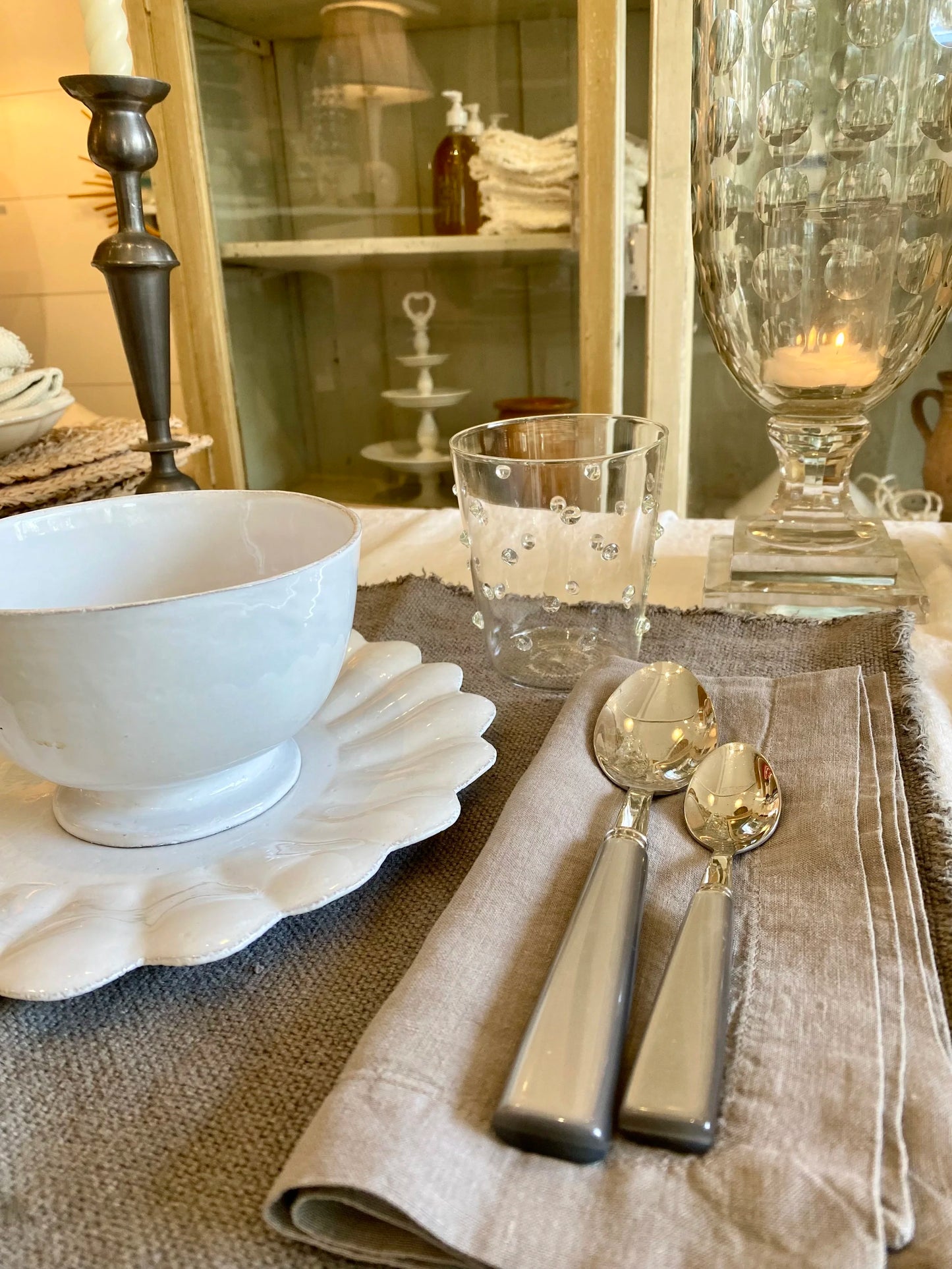Dining table setting with white bowl, glass, and silverware on a textured tablecloth with a tab napkin