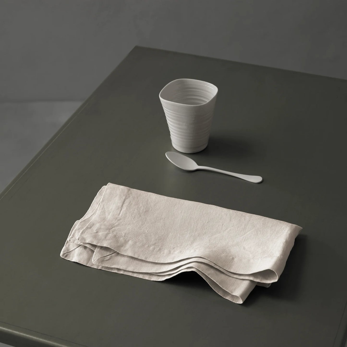 Gray ceramic cup, spoon, and folded napkin on a dark gray surface