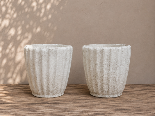 Two textured stone planters on a wooden surface with a neutral background