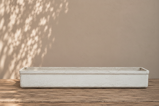 Rectangular concrete planter on a wooden surface with a beige wall in the background